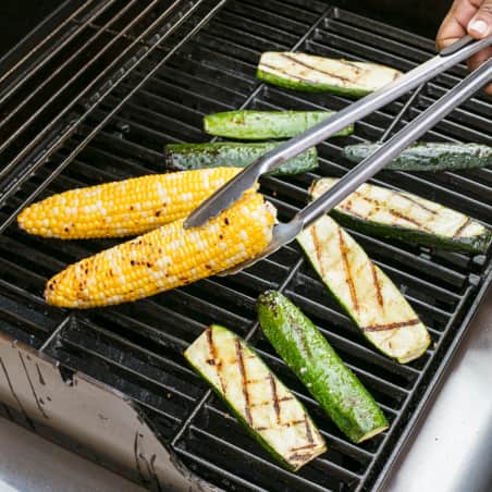 Planks of zucchini and ears of corn roasting on a gas grill. 